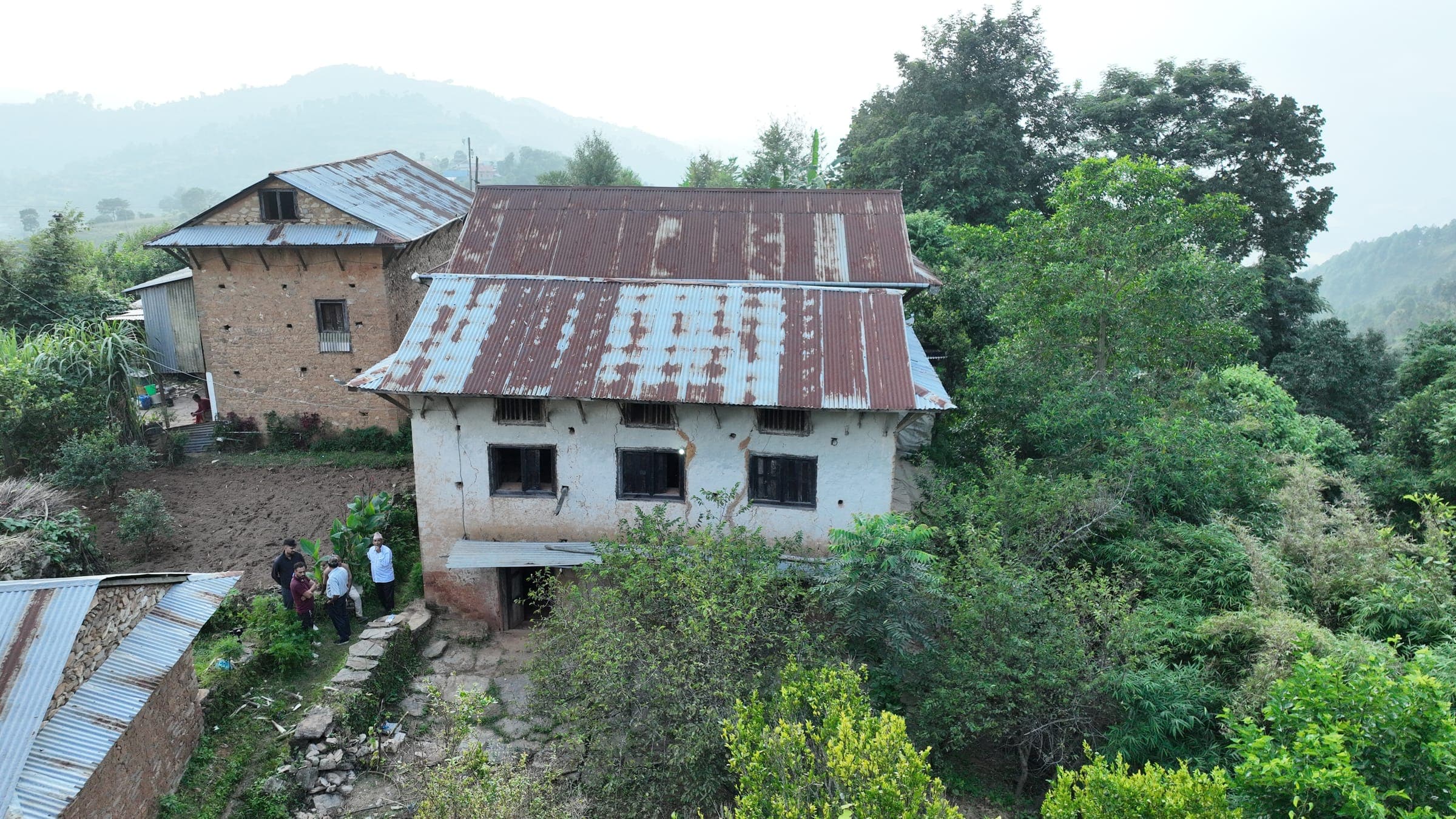 The old white house, overgrown on one side, with the family gathered in front on the first day of work, Bhadau 23, 2082