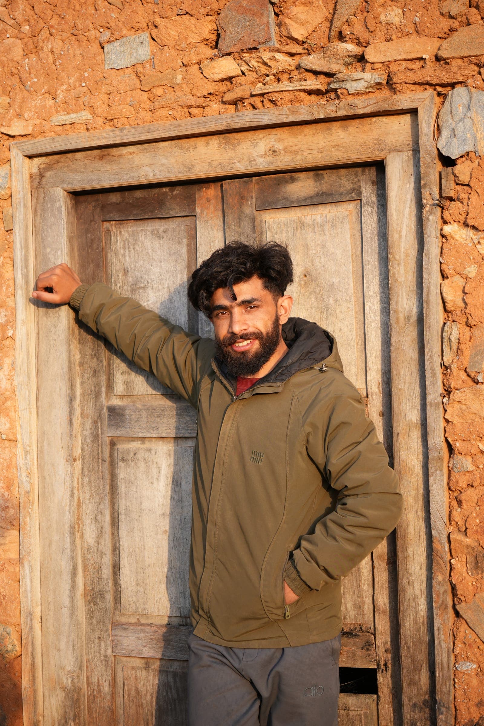A young man leaning against an old carved wooden door in the evening sun